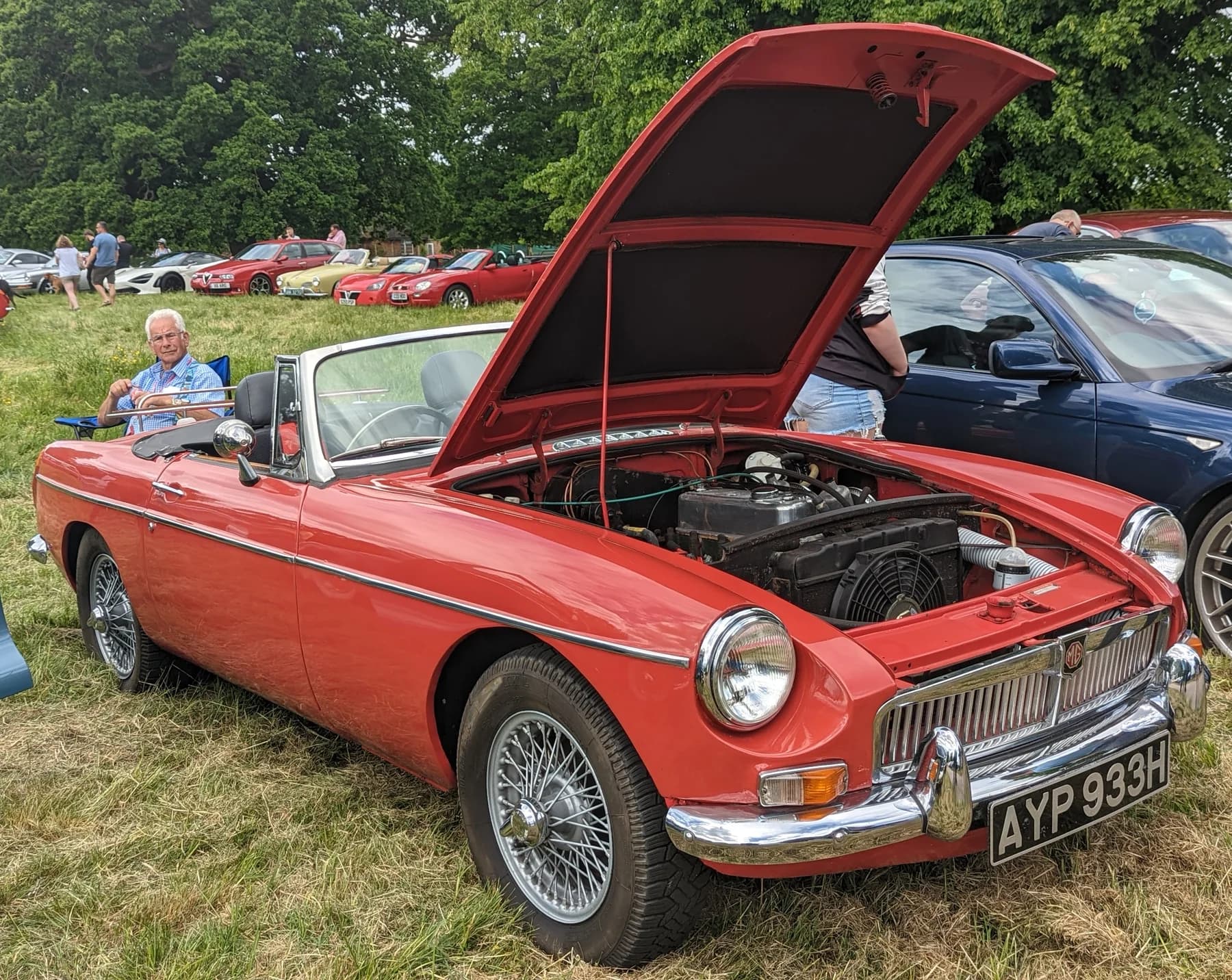 A red MGB roadster with its bonnet open at a car gathering