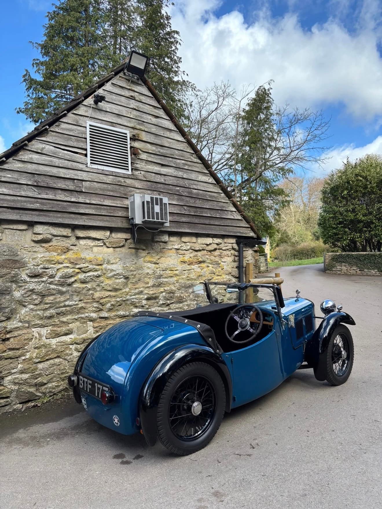 A blue vintage open-top car beside the stone building at The Rising Sun